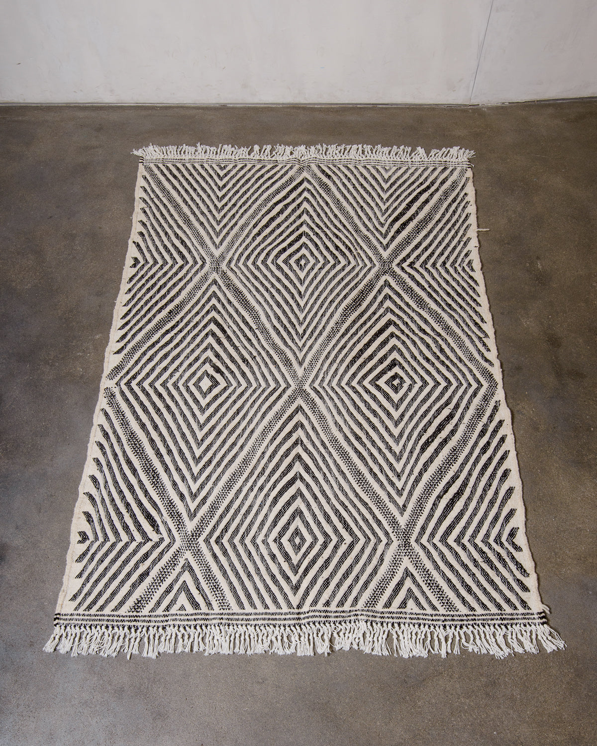 Black and white Kelim rug from Morocco laying on concrete floor.